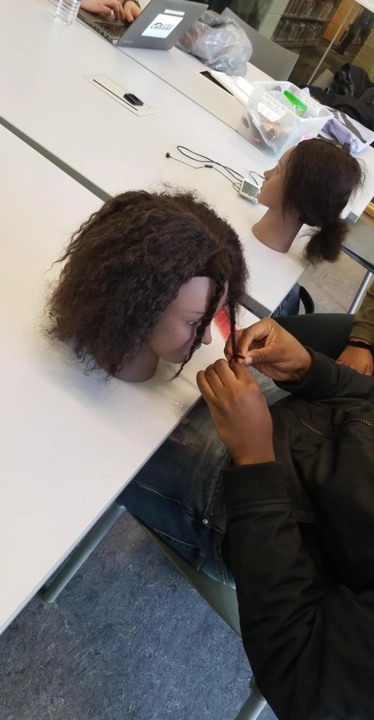 Participant practising a braid on a mannequin head at a learning table